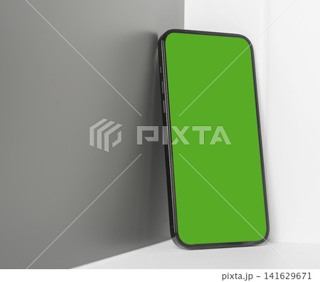 Smartphone mockup with a large bright green chroma key screen leans against a grey interior wall Smartphone mockup with a large bright green chroma key screen leans against a grey interior wall 141629671