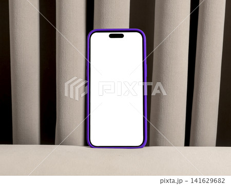 Smartphone with blank screen in purple case against curtain background. Vertical mobile device mockup with copy space in an indoor setting. App design and product presentation Smartphone with blank screen in purple case against curtain background. Vertical mobile device mockup with copy space in an indoor setting. App design and product presentation 141629682