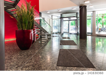 Modern office lobby with red feature wall and glass staircase, contemporary corporate interior with granite floor, cylindrical columns and large plant pots 141630360