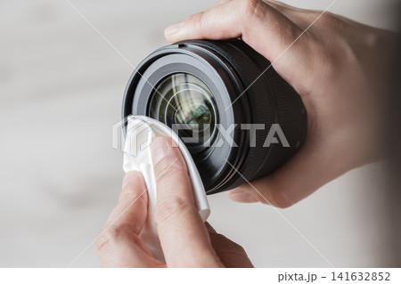 Person's hands carefully cleaning a camera lens with a white microfiber cloth Person's hands carefully cleaning a camera lens with a white microfiber cloth 141632852