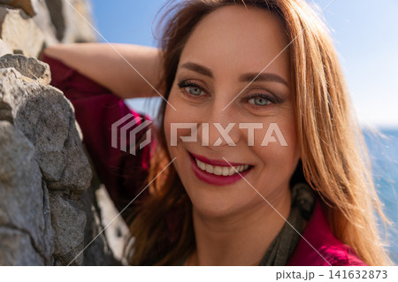 Woman smiling portrait beautiful adult female leaning against stone wall outdoors during sunny day enjoying her vacation Woman smiling portrait beautiful adult female leaning against stone wall outdoors during sunny day enjoying her vacation 141632873