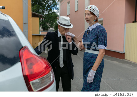 Elderly couple sharing a tender moment near a car in a quaint residential area during the afternoon Elderly couple sharing a tender moment near a car in a quaint residential area during the afternoon 141633017