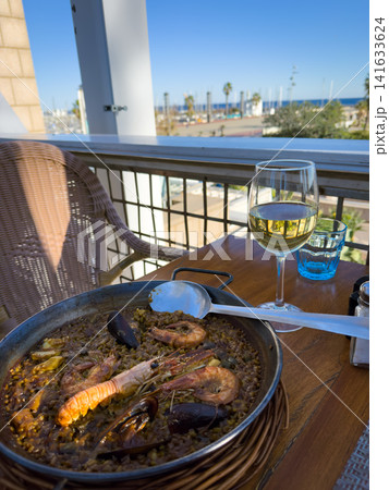 Seafood paella and white wine overlooking a marina Seafood paella and white wine overlooking a marina 141633624