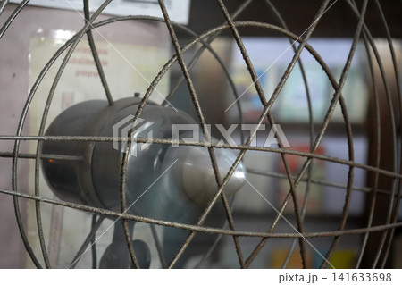 Close-Up Of Vintage Rusty Metal Fan Cage With Blurred Blades And Indoor Background Close-Up Of Vintage Rusty Metal Fan Cage With Blurred Blades And Indoor Background 141633698