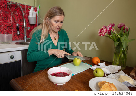 Woman prepares fruit in cozy kitchen while surrounded by fresh flowers and homemade treats Woman prepares fruit in cozy kitchen while surrounded by fresh flowers and homemade treats 141634043