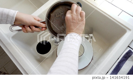 Man washes dishes in a kitchen sink 141634191