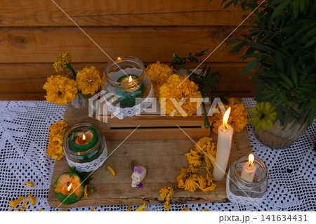 Marigold altar with lit candles in mason jars on wooden crate against wood wall and white crocheted cloth, bright orange flowers, lace wraps, warm memorial decor Marigold altar with lit candles in mason jars on wooden crate against wood wall and white crocheted cloth, bright orange flowers, lace wraps, warm memorial decor 141634431