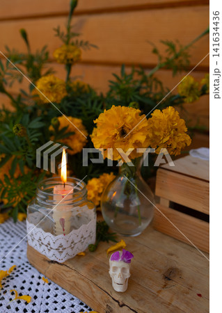Marigold altar arrangement with lit candle and decorative skull on rustic wooden table for memorial celebration, with day, dead, mexico, background detail, showing spanish, tradition, altar Marigold altar arrangement with lit candle and decorative skull on rustic wooden table for memorial celebration, with day, dead, mexico, background detail, showing spanish, tradition, altar 141634436
