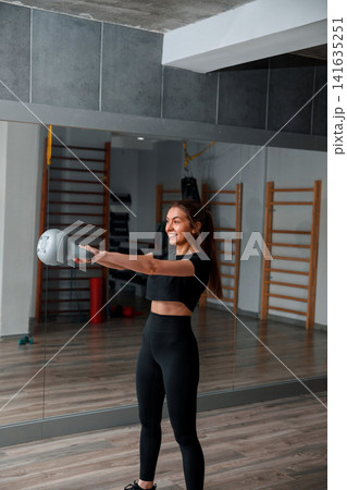 Woman exercises with a kettlebell in a gym setting during the day Woman exercises with a kettlebell in a gym setting during the day 141635251