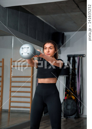 Woman exercises with a dumbbell in a gym during daylight focused on fitness and strength training routine Woman exercises with a dumbbell in a gym during daylight focused on fitness and strength training routine 141635252