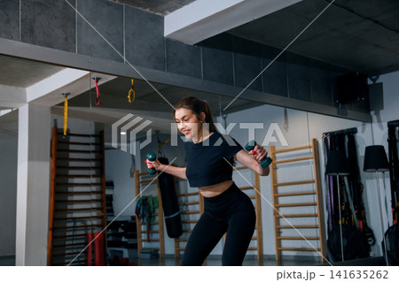 Beautiful woman exercising with dumbbells during energetic fitness workout. Young woman training upper body muscles inside modern gym interior. Strength wellness concept. Beautiful woman exercising with dumbbells during energetic fitness workout. Young woman training upper body muscles inside modern gym interior. Strength wellness concept. 141635262