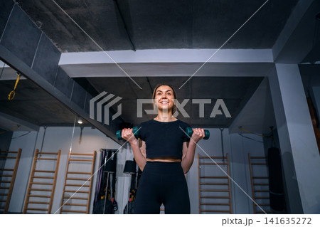 Beauty woman exercising with dumbbells during energetic fitness gym session. Attractive woman training indoors with healthy body posture and movement. Strength wellness concept. Beauty woman exercising with dumbbells during energetic fitness gym session. Attractive woman training indoors with healthy body posture and movement. Strength wellness concept. 141635272