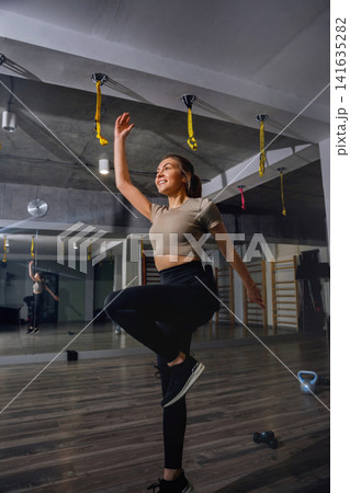 Woman practices fitness routine in gym area with mirrors and exercise equipment during daytime 141635282