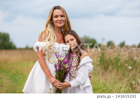 Mother and daughter share a joyful moment in a field with wildflowers on a sunny day Mother and daughter share a joyful moment in a field with wildflowers on a sunny day 141635291