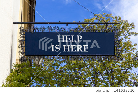 Help is here and support words symbol. Concept words Help is here on beautiful black road sign. Beautiful blue sky green tree background. Business help is here and support concept. Copy space. 141635310