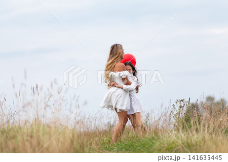 Mother and child enjoying a playful moment outdoors with a red balloon in a grassy field on a cloudy day Mother and child enjoying a playful moment outdoors with a red balloon in a grassy field on a cloudy day 141635445