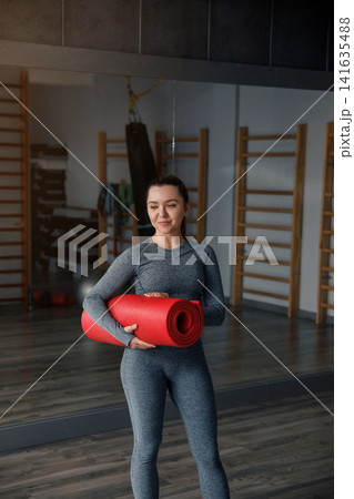 Woman fitness portrait holding red yoga mat in gym studio smiling with confidence and healthy lifestyle concept 141635488
