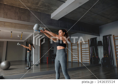 Woman fitness training indoors doing kettlebell swing movement in gym for strength power and healthy lifestyle Woman fitness training indoors doing kettlebell swing movement in gym for strength power and healthy lifestyle 141635514