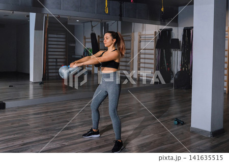Beauty woman exercising with kettlebell during focused indoor strength training. Attractive woman practicing athletic resistance workout with toned balanced posture indoors. Fitness wellness concept. Beauty woman exercising with kettlebell during focused indoor strength training. Attractive woman practicing athletic resistance workout with toned balanced posture indoors. Fitness wellness concept. 141635515