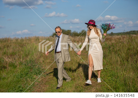 Couple walking hand in hand through a grassy field on a sunny day with colorful flowers 141635548