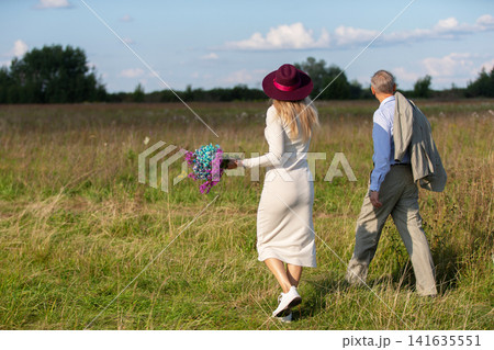 Couple enjoys a peaceful walk in a field during a sunny afternoon, celebrating nature and togetherness Couple enjoys a peaceful walk in a field during a sunny afternoon, celebrating nature and togetherness 141635551
