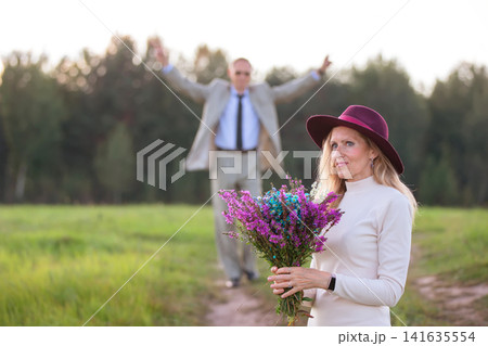 Couple enjoying a joyful moment outdoors with flowers in a scenic setting during golden hour Couple enjoying a joyful moment outdoors with flowers in a scenic setting during golden hour 141635554