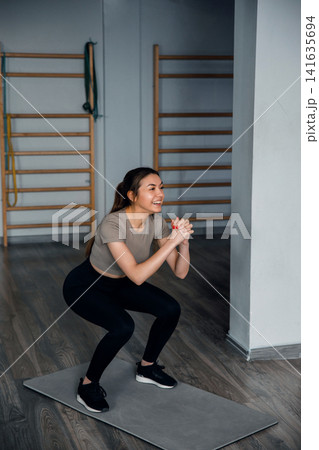 Beautiful woman doing squat exercise on mat in gym wearing sportswear with strength training and healthy fitness lifestyle concept Beautiful woman doing squat exercise on mat in gym wearing sportswear with strength training and healthy fitness lifestyle concept 141635694
