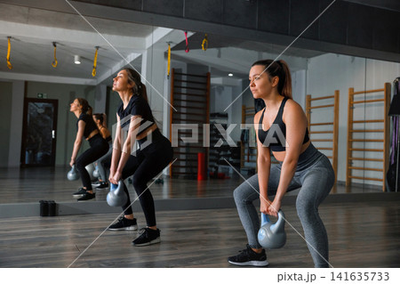 Women exercise with kettlebells in a gym during a workout session in the afternoon, focusing on strength training and fitness Women exercise with kettlebells in a gym during a workout session in the afternoon, focusing on strength training and fitness 141635733