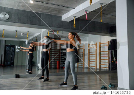 Woman exercises with kettlebell in gym during morning workout while looking at reflection in mirror 141635736
