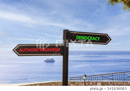 Democracy or authoritarianism symbol. Concept words Democracy Authoritarianism on beautiful black road sign. Beautiful blue sky background. Business democracy authoritarianism concept. Copy space Democracy or authoritarianism symbol. Concept words Democracy Authoritarianism on beautiful black road sign. Beautiful blue sky background. Business democracy authoritarianism concept. Copy space 141636063