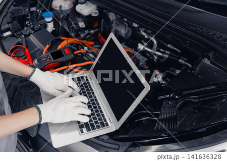 Professional EV Car Service, Worker Using Laptop Monitor Service EV Controller Inverter Diagnosis. Professional EV Car Service, Worker Using Laptop Monitor Service EV Controller Inverter Diagnosis. 141636328