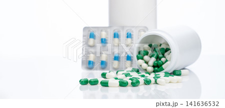 Green-white capsule pills on blur blister pack of blue-white capsule pills and drug bottle. Pills spread out of plastic bottle. Pharmaceutical industry. Prescription drug. Health and medical care. 141636532