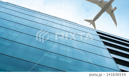 Airplane flying in the sky above modern sustainable glass office building. Exterior skyscraper green glass building. Business travel. Aviation business. Air logistics. Cargo plane. Departure flight. Airplane flying in the sky above modern sustainable glass office building. Exterior skyscraper green glass building. Business travel. Aviation business. Air logistics. Cargo plane. Departure flight. 141636554