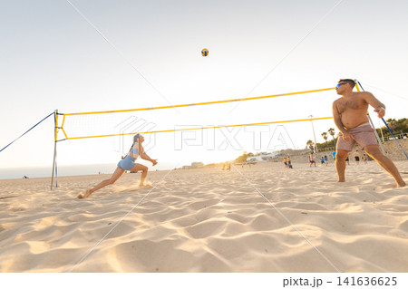People play beach volleyball at sunset near the shore with a net and sandy ground in the background during summer People play beach volleyball at sunset near the shore with a net and sandy ground in the background during summer 141636625
