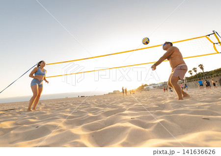 People play volleyball on the beach at sunset with a clear sky in the background and others nearby enjoying the evening People play volleyball on the beach at sunset with a clear sky in the background and others nearby enjoying the evening 141636626
