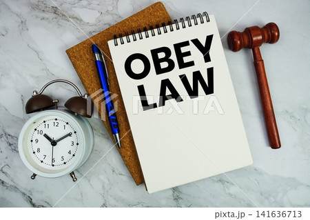 Obey Law text written on notepad with pen, alarm clock and judge gavel on marble background Obey Law text written on notepad with pen, alarm clock and judge gavel on marble background 141636713