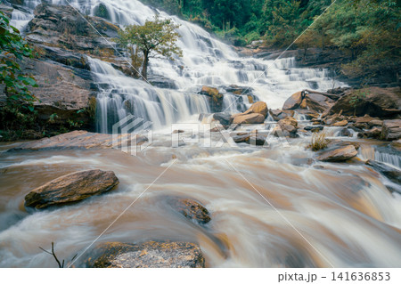 Beautiful waterfall with a lush green forest in the background. The water is flowing down the rocks and creating a beautiful scene. Sustainable waterfall in lush forest promoting water sustainability. Beautiful waterfall with a lush green forest in the background. The water is flowing down the rocks and creating a beautiful scene. Sustainable waterfall in lush forest promoting water sustainability. 141636853