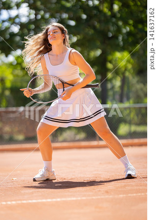 Tennis player practices on clay court in sunny weather during afternoon 141637162