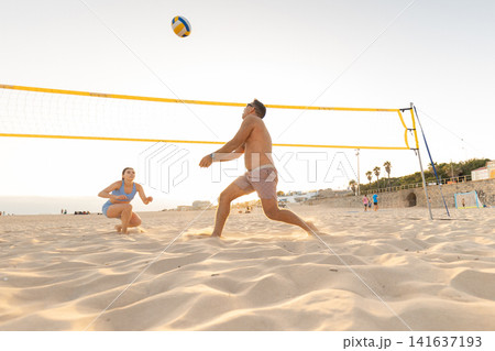 Beach volleyball match takes place at sunset on the sandy shore with players engaged in the game Beach volleyball match takes place at sunset on the sandy shore with players engaged in the game 141637193