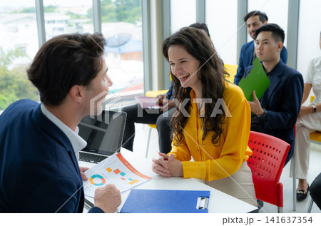 Business interview between a hiring manager and job candidate in modern office with colleagues in the background. Recruitment, communication, teamwork, career opportunities, and professional success. 141637354