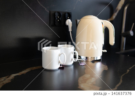 Modern electric kettle with white mugs on a kitchen counter Modern electric kettle with white mugs on a kitchen counter 141637376