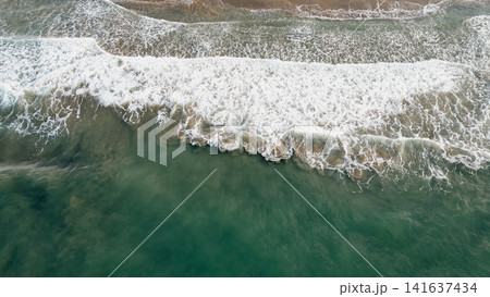 Top down aerial view of emerald sea waves washing ashore with white foam on sandy beach in Greece for ocean nature travel stock photo background concept texture Top down aerial view of emerald sea waves washing ashore with white foam on sandy beach in Greece for ocean nature travel stock photo background concept texture 141637434