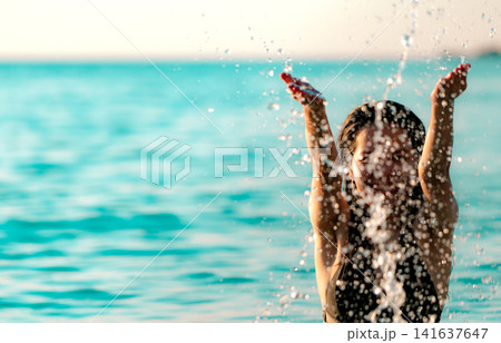 Happy woman splashing crystal clear seawater during tropical summer vacation, enjoying beach holiday, turquoise ocean, playful lifestyle, travel freedom and relaxing resort getaway. Luxury resort. Happy woman splashing crystal clear seawater during tropical summer vacation, enjoying beach holiday, turquoise ocean, playful lifestyle, travel freedom and relaxing resort getaway. Luxury resort. 141637647