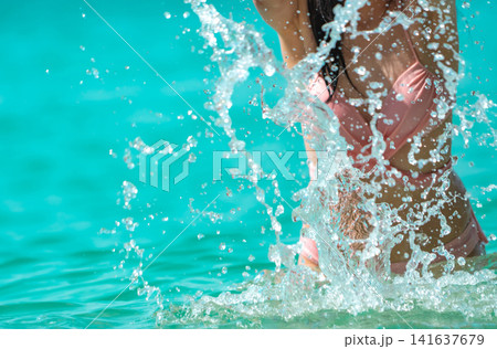 Dynamic close up of woman splashing crystal clear turquoise seawater during a tropical summer beach vacation, refreshing holiday lifestyle, energetic travel banner. Active beach lifestyle, recreation. Dynamic close up of woman splashing crystal clear turquoise seawater during a tropical summer beach vacation, refreshing holiday lifestyle, energetic travel banner. Active beach lifestyle, recreation. 141637679