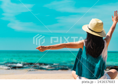 Back view of happy woman raising her arms toward the turquoise tropical ocean on a sunny summer beach. Freedom, wellness lifestyle, travel adventure and vacation. Wellness retreat, travel destination. Back view of happy woman raising her arms toward the turquoise tropical ocean on a sunny summer beach. Freedom, wellness lifestyle, travel adventure and vacation. Wellness retreat, travel destination. 141637683