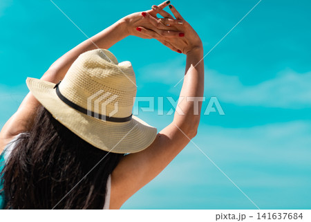 Woman stretching under a bright blue sky on a tropical beach during a relaxing summer vacation. Wellness, mindfulness, healthy lifestyle, travel freedom. Self care, wellness vacation, coastal travel. 141637684