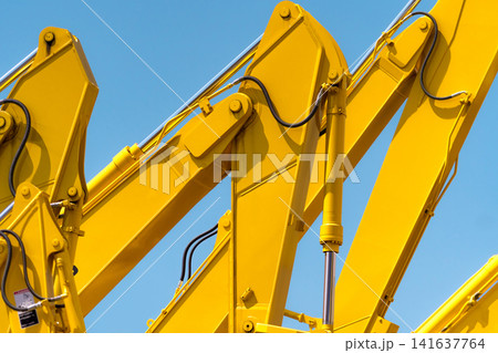 Closeup yellow hydraulic excavator arm with piston cylinder against blue sky, heavy construction machinery, industrial engineering equipment and mechanical technology background. Mechanical industry. Closeup yellow hydraulic excavator arm with piston cylinder against blue sky, heavy construction machinery, industrial engineering equipment and mechanical technology background. Mechanical industry. 141637764