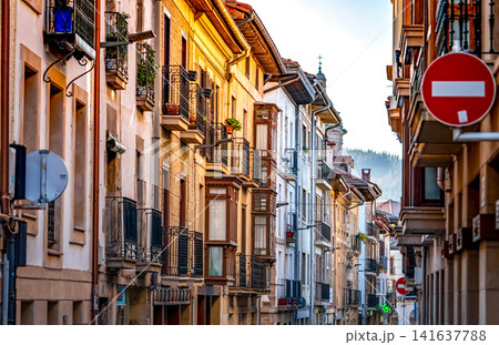 Traditional residential buildings along a narrow street in Spain. Classic European architecture, historic urban neighborhood, balconies and morning sunlight in an old town. Scenic travel destination. Traditional residential buildings along a narrow street in Spain. Classic European architecture, historic urban neighborhood, balconies and morning sunlight in an old town. Scenic travel destination. 141637788