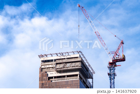 Tower crane constructing high rise building against blue sky. Urban development, commercial construction and infrastructure growth. Engineering, real estate development and modern city expansion. Tower crane constructing high rise building against blue sky. Urban development, commercial construction and infrastructure growth. Engineering, real estate development and modern city expansion. 141637920