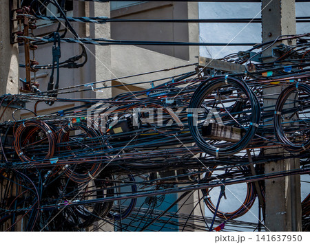 Tangled electrical and telecommunications cables on urban utility pole. Disorganized overhead infrastructure, fiber optic network installation and city power distribution management. Tangled electrical and telecommunications cables on urban utility pole. Disorganized overhead infrastructure, fiber optic network installation and city power distribution management. 141637950